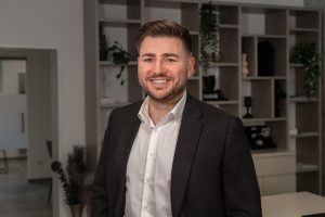 Danny Anzinger, Immobilienberater bei David Deindl Immobilien, lächelnd im Büro